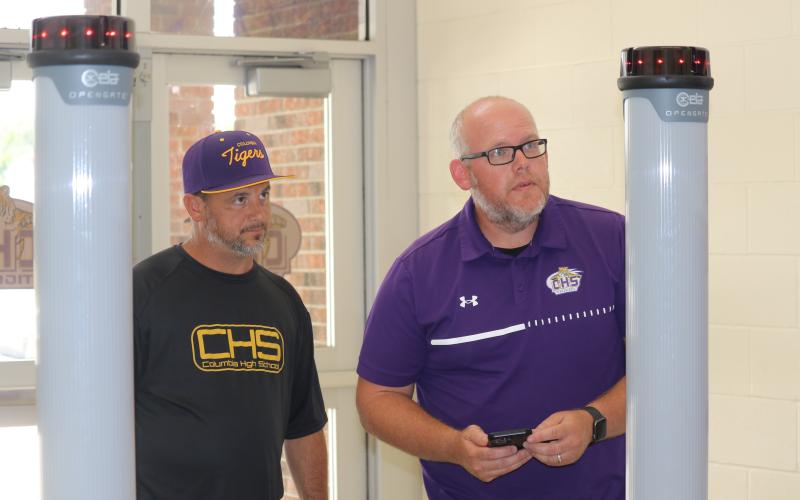 Columbia High Principal Trey Hosford (left) and Assistant Principal Doug Peeler test one of the portable metal detectors Monday at the CHS front entrance. (JAMIE WACHTER/Lake City Reporter)