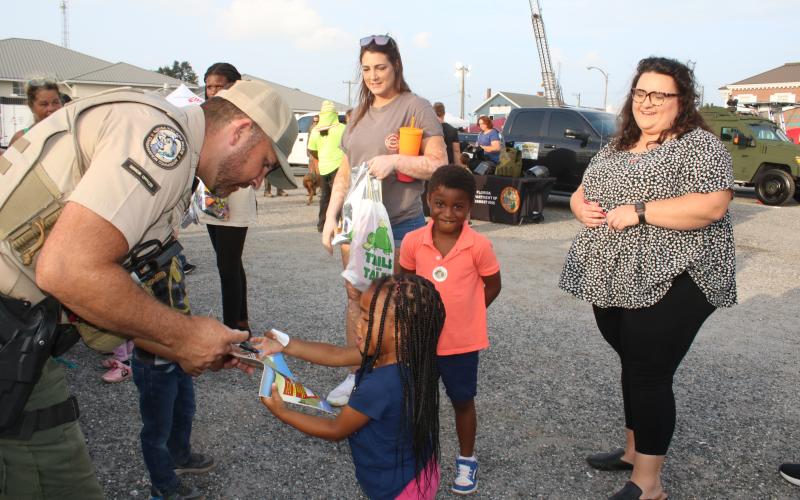 Luke Davenport, a Florida Fish and Conservation Commission officer, signs a coloring book for Ava Flores, 2, as Elias Flores, 4 and Chelsea Flores (far right) look on. (TONY BRITT/Lake City Reporter)