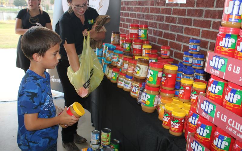 Paul Westridge, 7, helps Adrienne Metcalf align jars of peanut butter that were donated during the second Farm to Table event. The event, which honors Columbia County’s agricultural history, took place Thursday evening at Darby Pavilion. (TONY BRITT/Lake City Reporter)