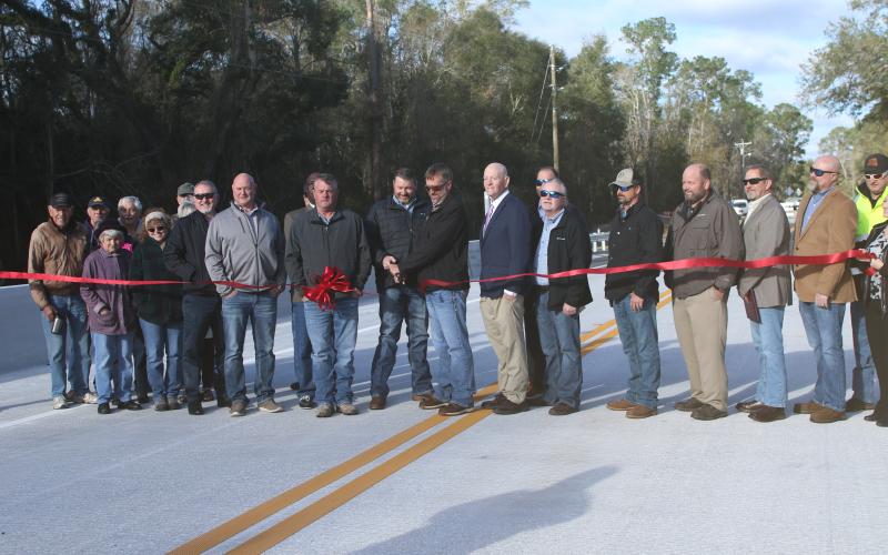 Suwannee County Commissioners Travis Land and Leo Mobley (middle) cut the ribbon Monday marking the reopening of the 180th Street bridge across Little River. (JAMIE WACHTER/Lake City Reporter)