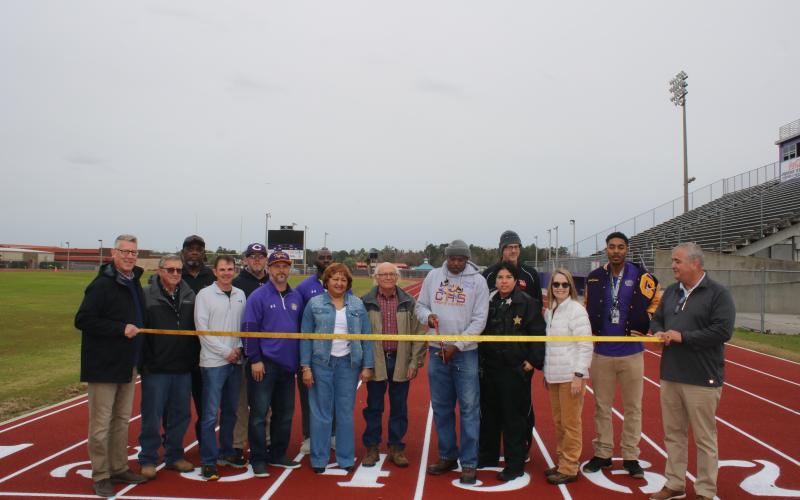 Columbia County School District administrators, Columbia County School Board members and Columbia High School representatives look on as CHS track coach Lawrence Davis cuts the ribbon Monday to officially open the resurfaced track at Tiger Stadium. (TONY BRITT/Lake City Reporter)