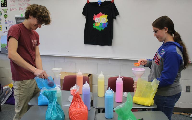 Brody Crews (left) and Isabel Heeke, Fort White High School National Honor Society club officers, fill dispensers with paint for the club’s color fun run that will take place on Saturday at the school’s football stadium. (TONY BRITT/Lake City Reporter)