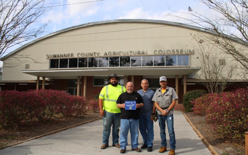 Rapid Fiber Internet Vice President of System Operations Chris McKenzie holds up a ‘Free Wi-Fi’ sign in front of the Suwannee County Coliseum after EnterSource, Rapid Fiber’s installation contractor, added the service to the public facility. EnterSource staff are pictured with McKenzie. (COURTESY)