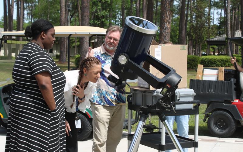 Jessica Ervienn (middle) squints as she looks through a telescope to watch Monday’s solar eclipse as she gets tips from FGC physics professor James Givviens. (TONY BRITT/Lake City Reporter)