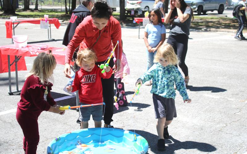 Aniya Woodcock (from left), 4, Khalil Williams, 2, and Parker Pemberton, 4, get help from Katie Stewart as the youngsters play a game attempting to catch plastic fish at the Spring Family Fun Day at Ichetuckee Springs State Park on Saturday. (TONY BRITT/Lake City Reporter)